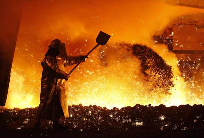 Worker in protective gear shoveling material in a fiery industrial furnace